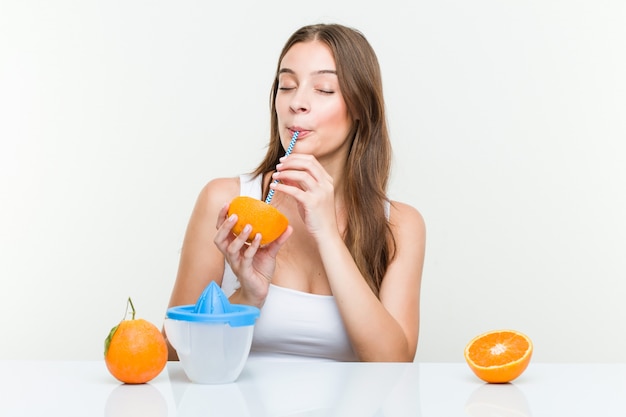 Jonge blanke vrouw die een sinaasappel met een rietje drinkt.