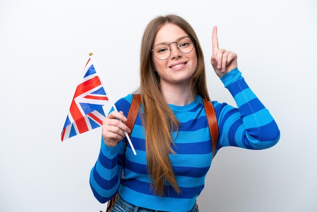 Jonge blanke vrouw die een vlag van het Verenigd Koninkrijk houdt die op witte achtergrond wordt geïsoleerd die een geweldig idee benadrukt