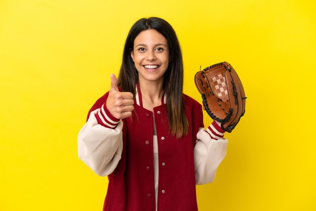 Jonge blanke vrouw die honkbal speelt geïsoleerd op gele achtergrond met duimen omhoog omdat er iets goeds is gebeurd