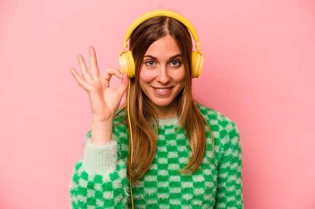 Jonge blanke vrouw die naar muziek luistert geïsoleerd op een roze achtergrond, vrolijk en zelfverzekerd met een goed gebaar