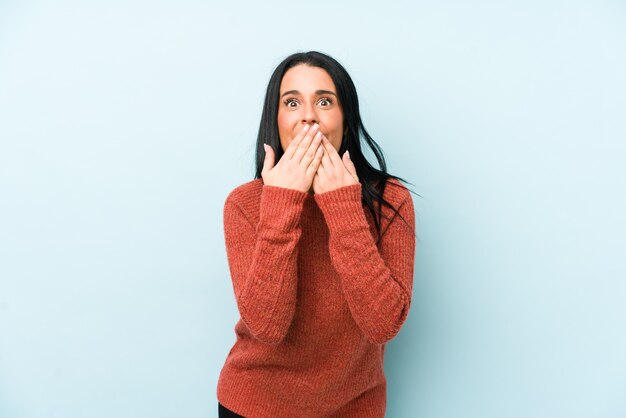 Jonge blanke vrouw die op een blauwe geschokt die mond behandelt met handen.