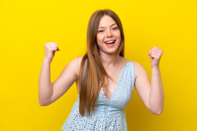 Jonge blanke vrouw die op gele achtergrond wordt geïsoleerd die een overwinning in winnaarpositie viert