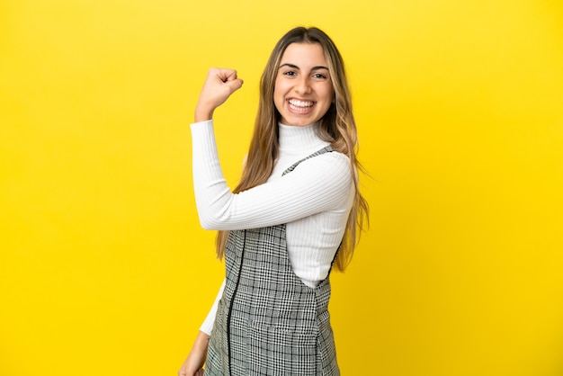 Jonge blanke vrouw die op gele achtergrond wordt geïsoleerd die een overwinning viert