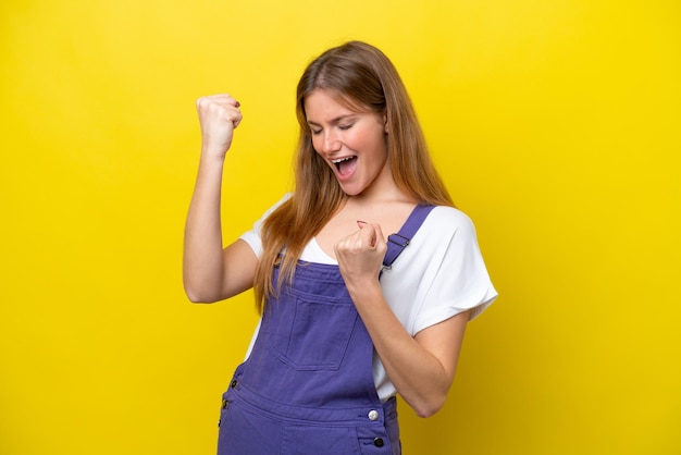 Jonge blanke vrouw die op gele achtergrond wordt geïsoleerd die een overwinning viert