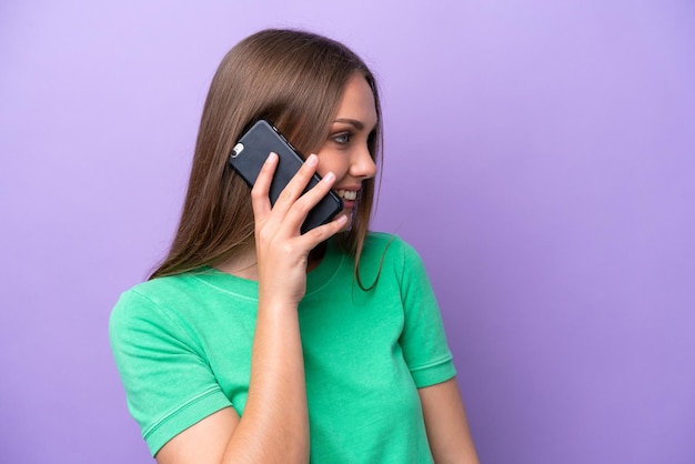 Jonge blanke vrouw die op paarse achtergrond een gesprek met de mobiele telefoon met iemand houdt