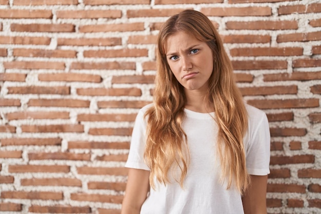 Jonge blanke vrouw die over de bakstenen muur staat en er slaperig en moe uitziet, uitgeput van vermoeidheid en kater, luie ogen in de ochtend.