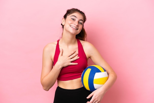 Jonge blanke vrouw die volleybal speelt geïsoleerd op een roze achtergrond die veel lacht