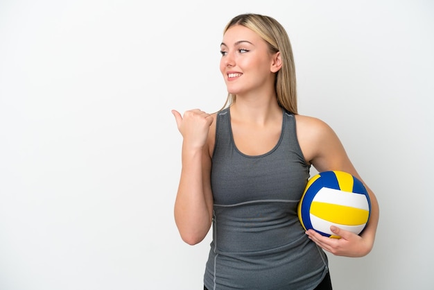 Jonge blanke vrouw die volleybal speelt geïsoleerd op een witte achtergrond, wijzend naar de zijkant om een product te presenteren