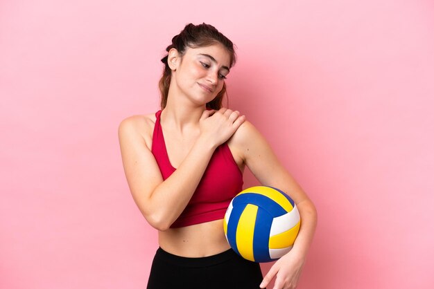 Jonge blanke vrouw die volleybal speelt geïsoleerd op roze achtergrond die lijdt aan pijn in de schouder omdat ze zich heeft ingespannen