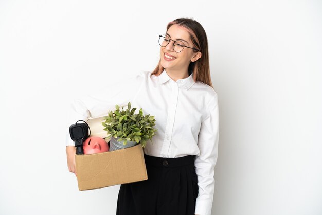 Jonge blanke vrouw die zich in een nieuw huis onder de dozen beweegt die op een witte achtergrond naar de zijkant kijken en glimlachen