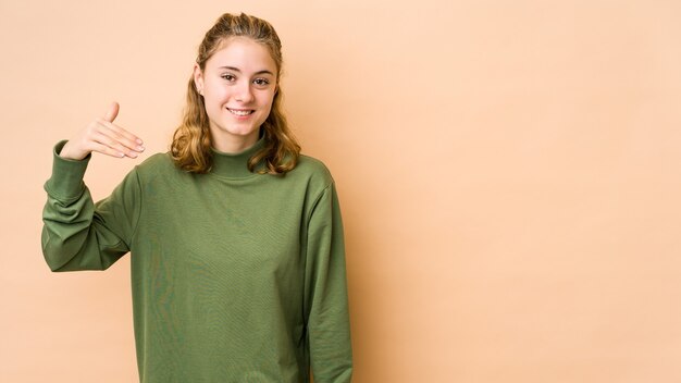 Jonge blanke vrouw geïsoleerd in beige lachen om iets, mond bedekken met handen.