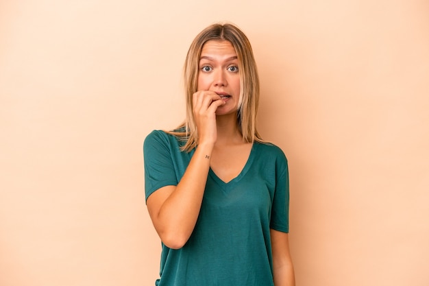 Jonge blanke vrouw geïsoleerd op beige achtergrond bijtende vingernagels, nerveus en erg angstig.