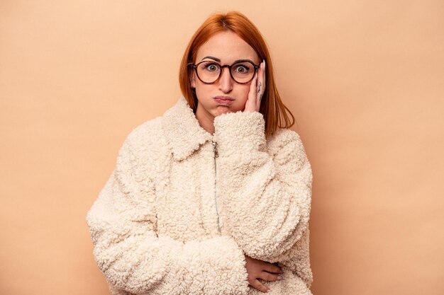 Jonge blanke vrouw geïsoleerd op beige achtergrond blaast wangen heeft vermoeide uitdrukking Gezichtsuitdrukking concept