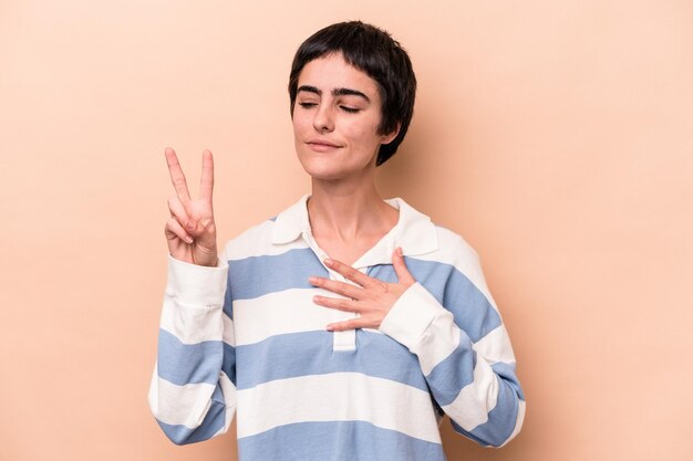 Jonge blanke vrouw geïsoleerd op beige achtergrond die een eed aflegt, hand op de borst.