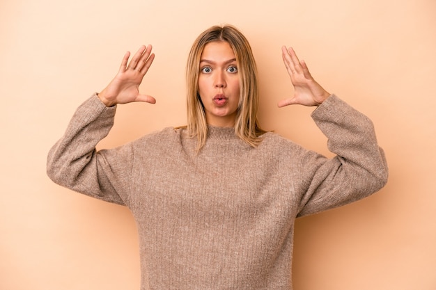 Foto jonge blanke vrouw geïsoleerd op beige achtergrond die een overwinning of succes viert, hij is verrast en geschokt.