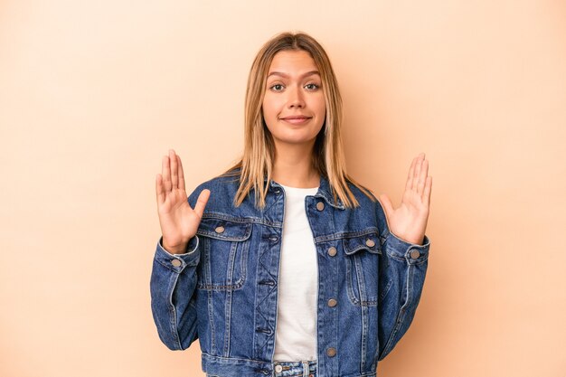 Jonge blanke vrouw geïsoleerd op beige achtergrond met iets kleins met wijsvingers, glimlachend en zelfverzekerd.