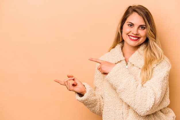 Jonge blanke vrouw geïsoleerd op beige achtergrond opgewonden wijzend met wijsvingers weg