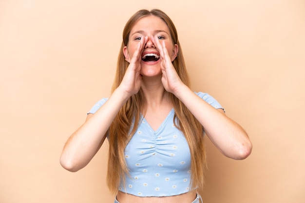 Jonge blanke vrouw geïsoleerd op beige achtergrond schreeuwen en iets aankondigen