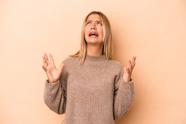 Jonge blanke vrouw geïsoleerd op beige achtergrond schreeuwen naar de hemel, opzoeken, gefrustreerd.