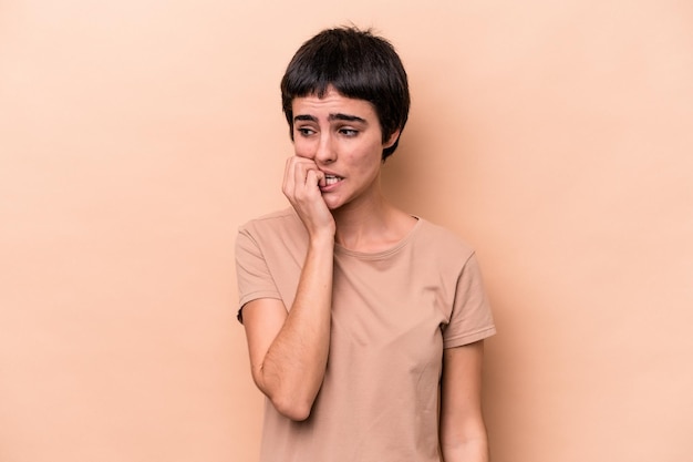 Jonge blanke vrouw geïsoleerd op beige achtergrond vingernagels bijten nerveus en erg angstig