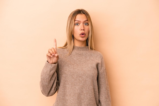 Jonge blanke vrouw geïsoleerd op beige achtergrond wijzend ondersteboven met geopende mond.