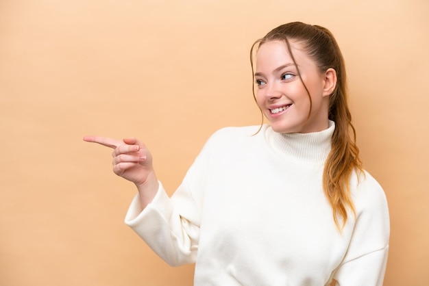 Jonge blanke vrouw geïsoleerd op beige achtergrond wijzende vinger naar de zijkant en een product presenteren