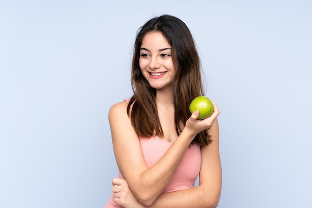 Jonge blanke vrouw geïsoleerd op blauw met een appel en gelukkig