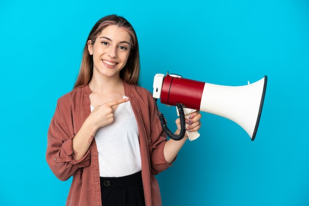 Jonge blanke vrouw geïsoleerd op blauw met een megafoon en een wijzende kant