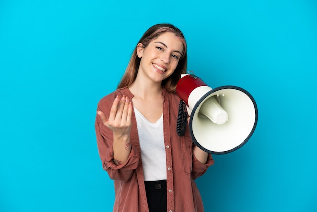 Jonge blanke vrouw geïsoleerd op blauw met een megafoon en uitnodigend om met de hand te komen