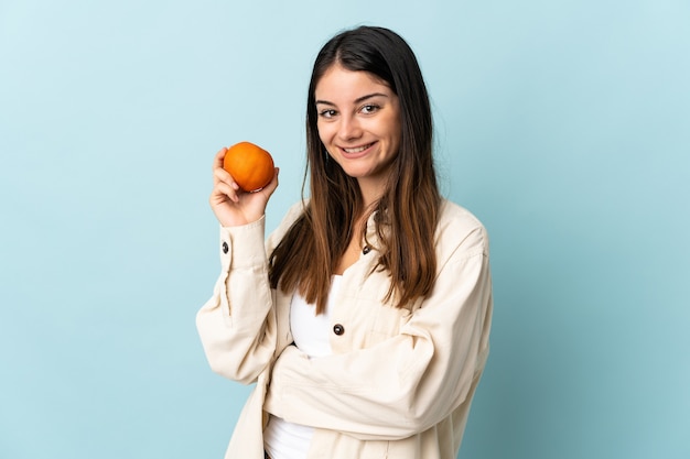 Jonge blanke vrouw geïsoleerd op blauw met een sinaasappel
