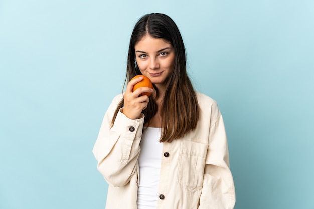 Jonge blanke vrouw geïsoleerd op blauw met een sinaasappel