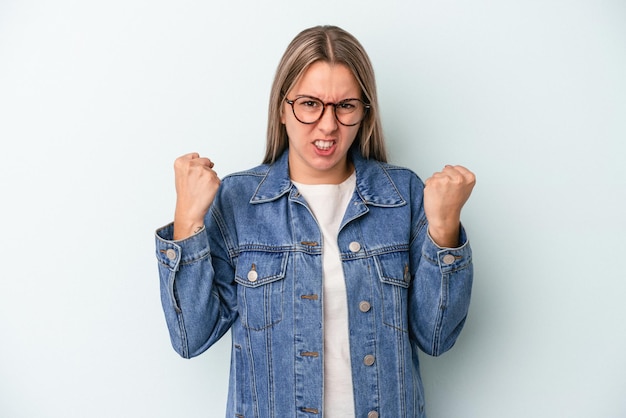 Jonge blanke vrouw geïsoleerd op blauwe achtergrond boos schreeuwen met gespannen handen.