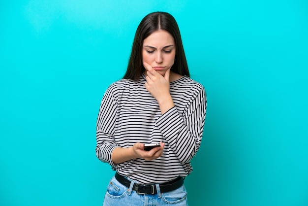 Jonge blanke vrouw geïsoleerd op blauwe achtergrond denken en een bericht verzenden