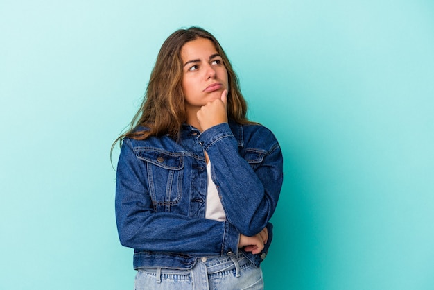 Jonge blanke vrouw geïsoleerd op blauwe achtergrond denken en opzoeken, reflecterend zijn, nadenken, een fantasie hebben.