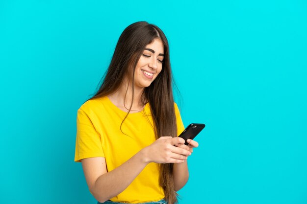 Jonge blanke vrouw geïsoleerd op blauwe achtergrond die een bericht verzendt met de mobiel