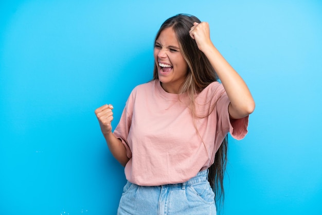 Jonge blanke vrouw geïsoleerd op blauwe achtergrond die een overwinning viert