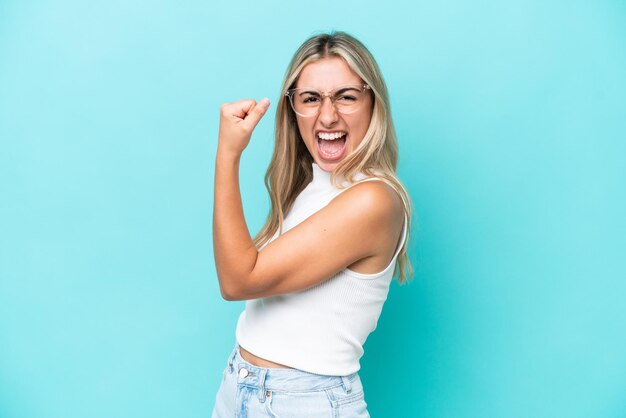 Jonge blanke vrouw geïsoleerd op blauwe achtergrond die een overwinning viert