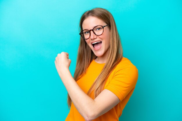 Jonge blanke vrouw geïsoleerd op blauwe achtergrond die een overwinning viert