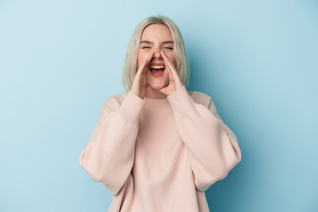 Jonge blanke vrouw geïsoleerd op blauwe achtergrond die een roddel zegt, wijzend naar de zijkant die iets meldt.