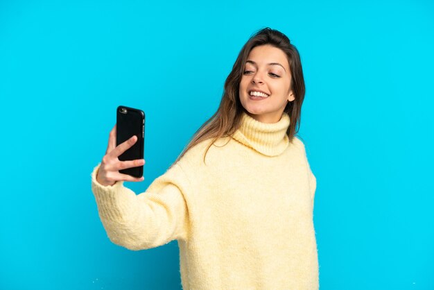 Jonge blanke vrouw geïsoleerd op blauwe achtergrond die een selfie maakt