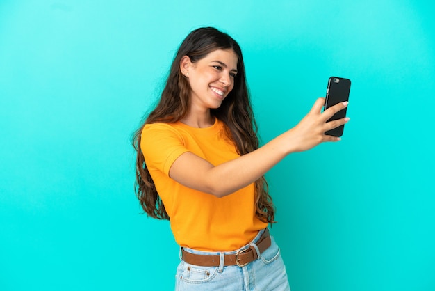 Jonge blanke vrouw geïsoleerd op blauwe achtergrond die een selfie maakt