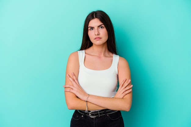 Jonge blanke vrouw geïsoleerd op blauwe achtergrond fronsend gezicht in ongenoegen, houdt armen gevouwen.