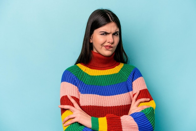 Jonge blanke vrouw geïsoleerd op blauwe achtergrond fronsend gezicht in ongenoegen houdt armen over elkaar