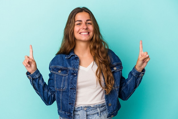 Jonge blanke vrouw geïsoleerd op blauwe achtergrond geeft aan dat met beide voorvingers een lege ruimte wordt weergegeven.