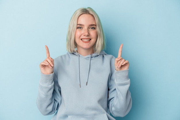 Jonge blanke vrouw geïsoleerd op blauwe achtergrond geeft aan dat met beide voorvingers een lege ruimte wordt weergegeven.