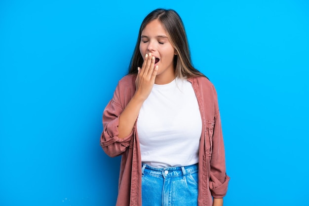 Jonge blanke vrouw geïsoleerd op blauwe achtergrond geeuwen en wijd open mond met hand bedekken