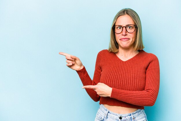 Foto jonge blanke vrouw geïsoleerd op blauwe achtergrond geschokt wijzend met wijsvingers naar een kopie ruimte