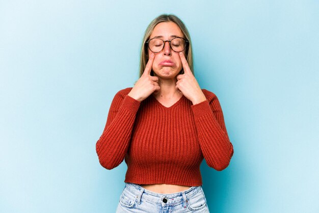 Jonge blanke vrouw geïsoleerd op blauwe achtergrond huilen ongelukkig met iets pijn en verwarring concept