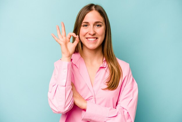 Jonge blanke vrouw geïsoleerd op blauwe achtergrond knipoogt en houdt een goed gebaar met de hand