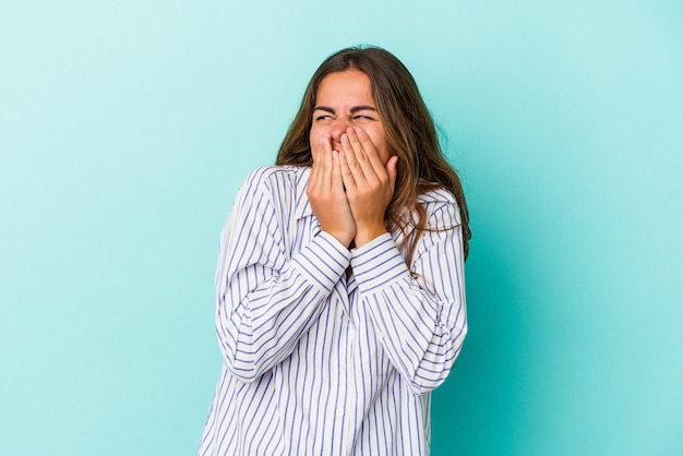 Jonge blanke vrouw geïsoleerd op blauwe achtergrond lachen om iets, mond bedekken met handen.